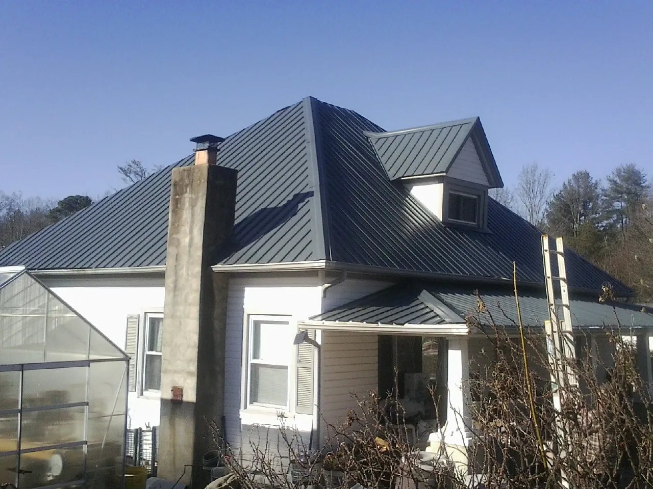 Dark blue standing seam metal roof on a white farmhouse with dormer — Slate & Tile Roof Repair by Roofing Brothers in Crooks