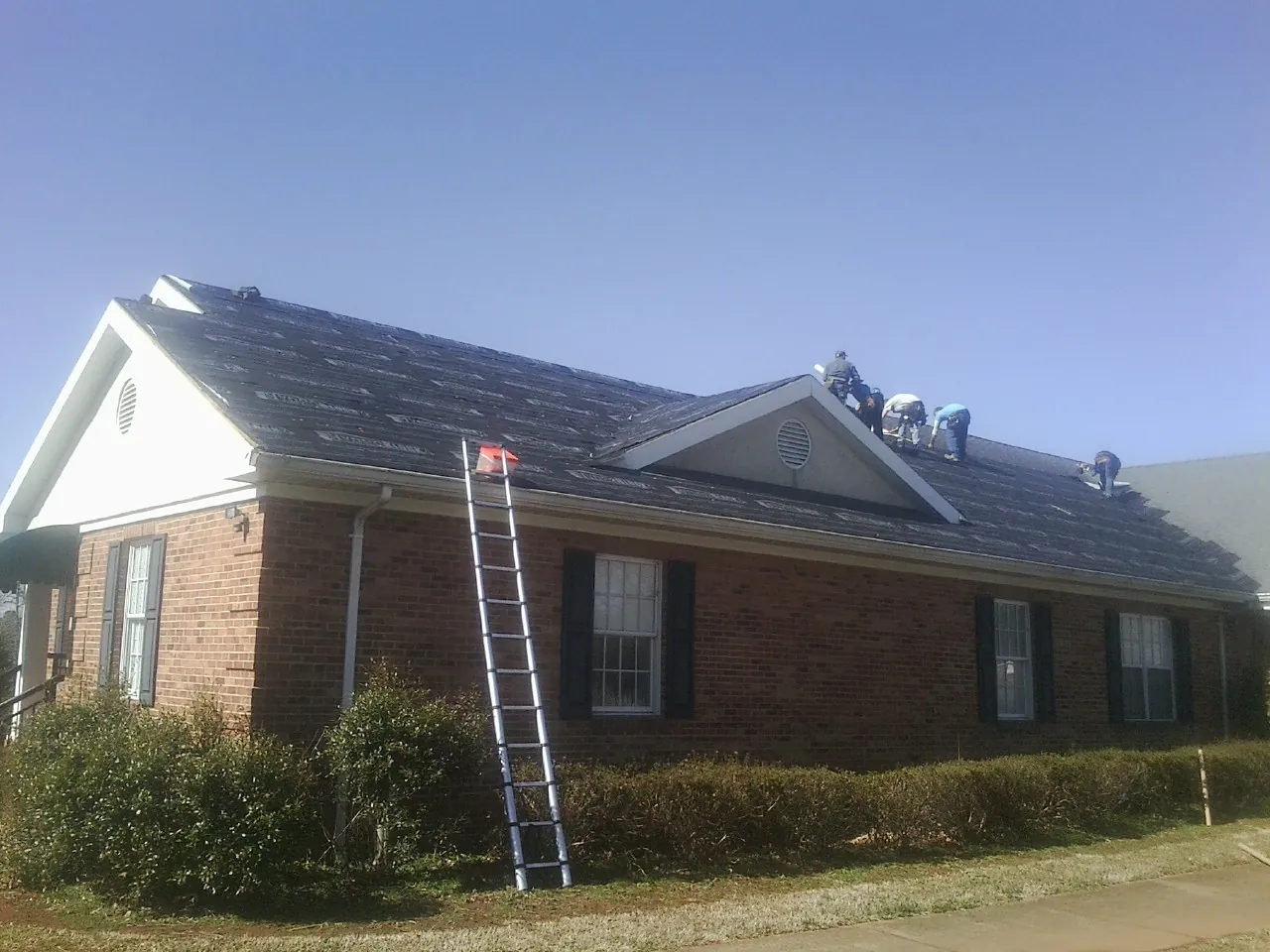 Crew tearing shingles off a brick ranch roof with a ladder set — Emergency Roof Repair work by our crew in Crooks