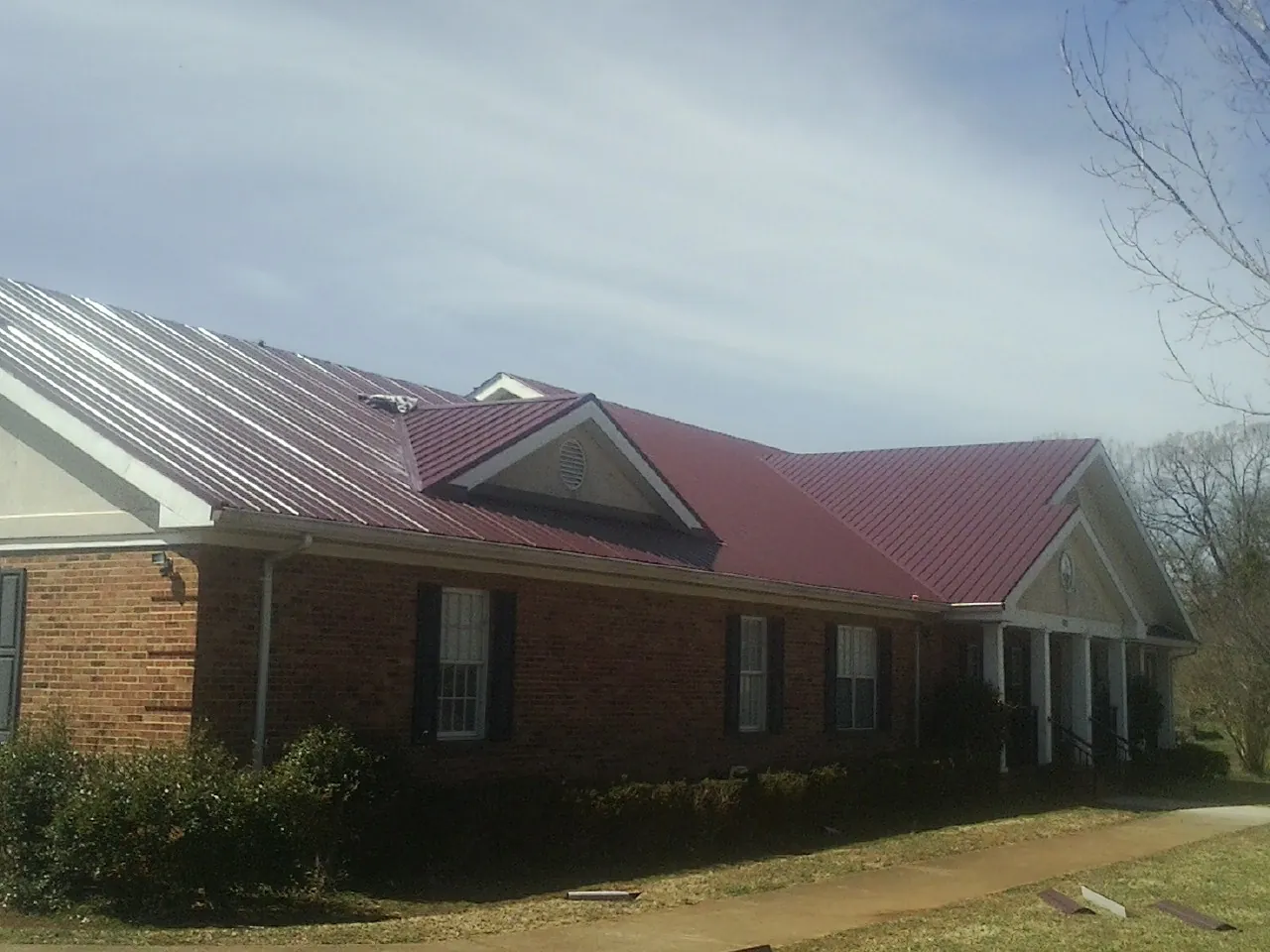 Red metal roof with gabled entries on a long brick building, from a Hail Damage Roof Repair job in Crooks