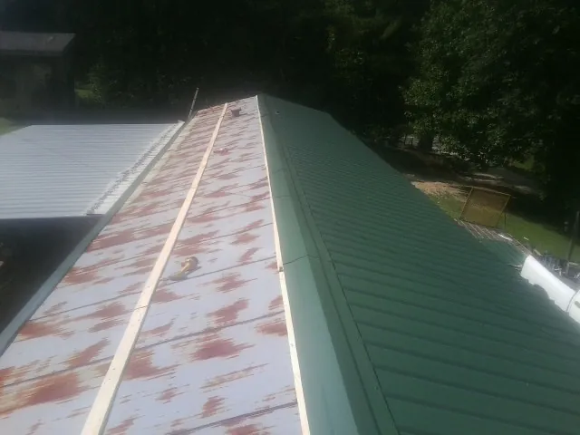 Old rusted panels beside newly installed green metal roofing — Wind Damage Roof Repair by Roofing Brothers in Crooks