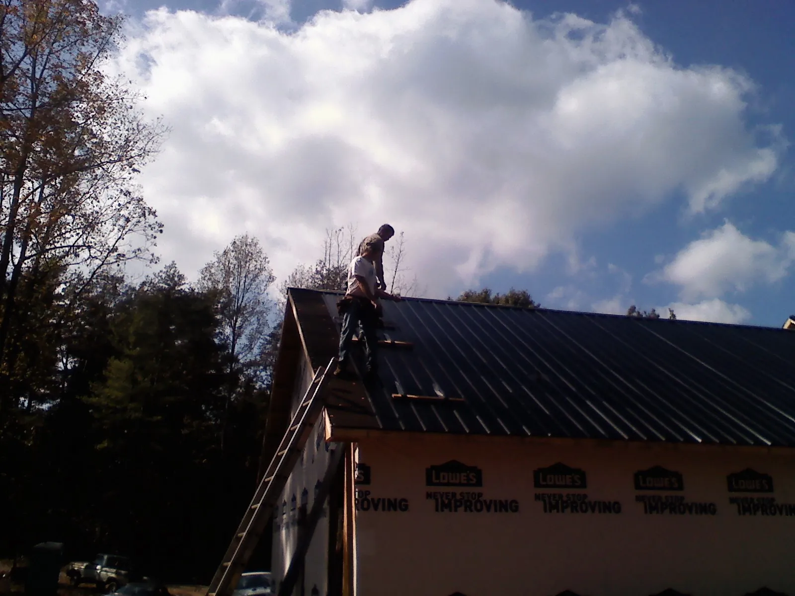 Roofer fastening dark metal panels high against a cloudy sky, from a Roof Inspection job in Crooks