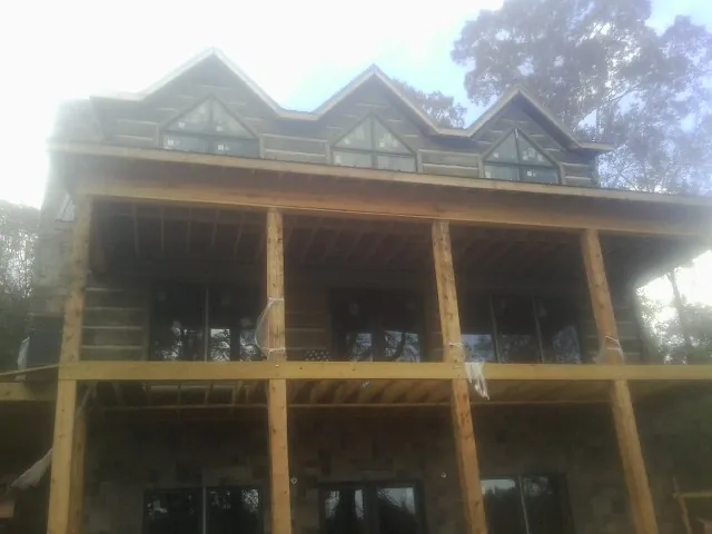 Dormers and porch framing on a large log home under construction — Roof Coating work by our crew in Crooks