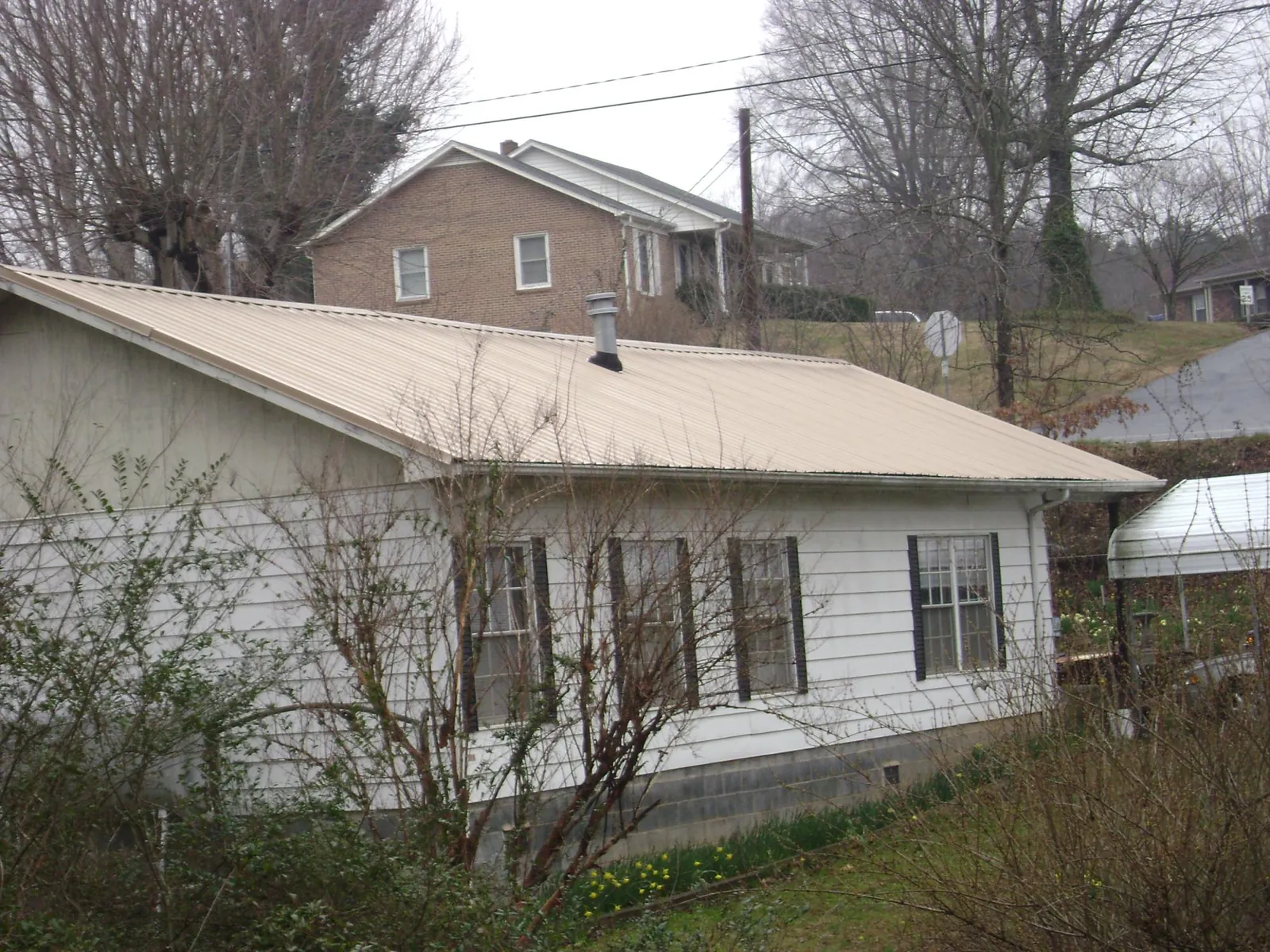 Tan metal roof on a white sided house set into a hillside — Commercial Roofing by Roofing Brothers in Crooks