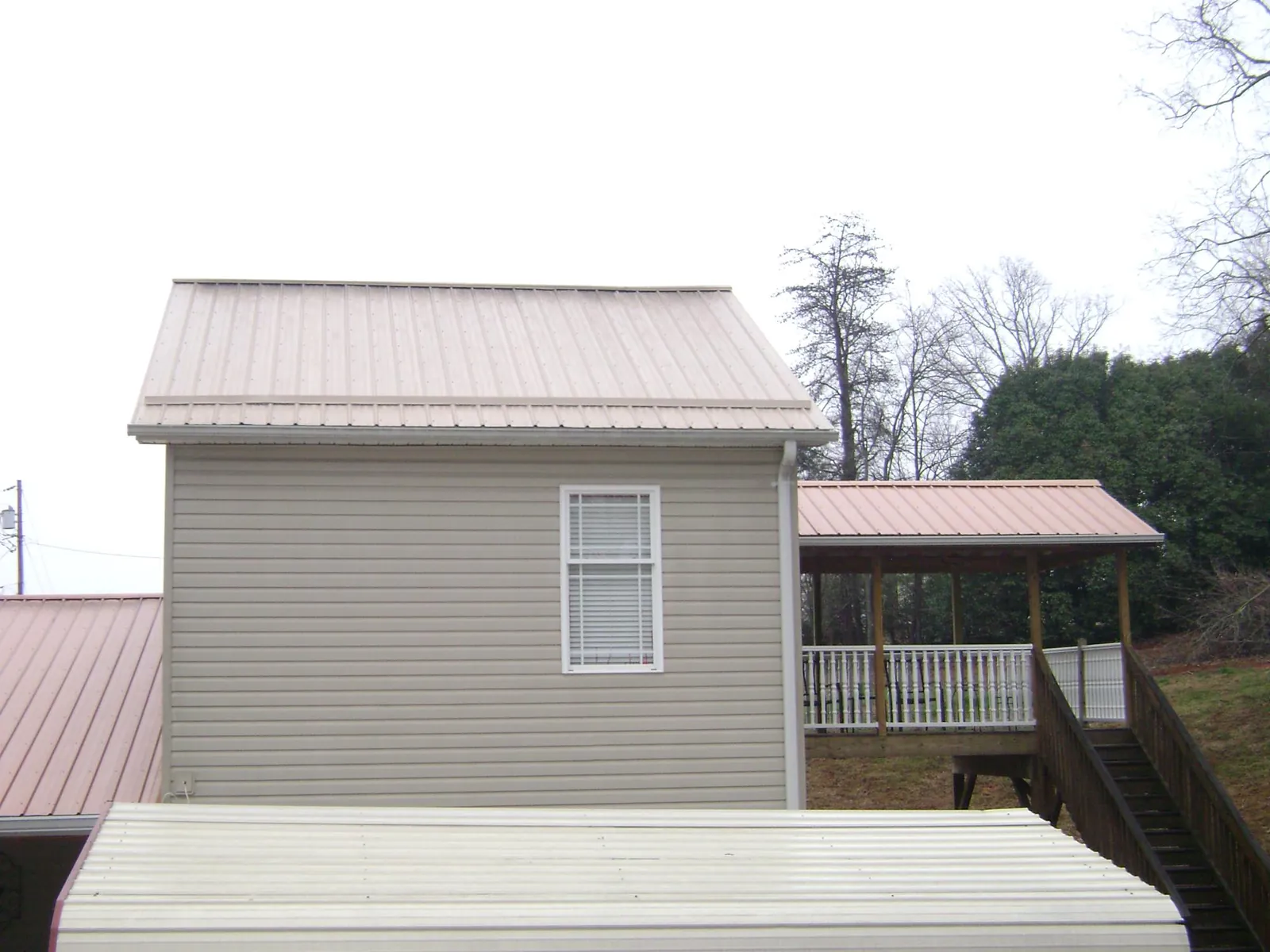 Tan metal roofs on a two story addition and attached porch, from a Roof Replacement job in Crooks